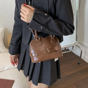 Detail of a brown glossy shell bag with bow decoration and polished metal eyelets