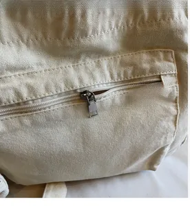 Detailed close-up of smooth silver zipper and stitching on the off-white canvas tote bag