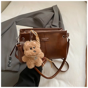 Détail du sac bandoulière vintage marron avec charm chien en peluche et plaque dorée