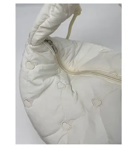 Détail de la fermeture éclair argentée et motif cœur matelassé sur le sac blanc