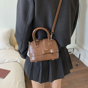 Brown PU leather shell bag with bow detail shown in a cozy indoor lifestyle setting