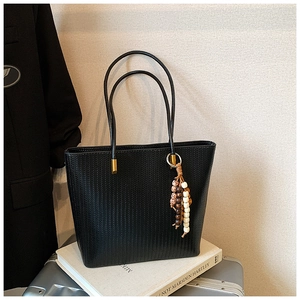 Dettaglio della borsa tote nera intrecciata con fibbie dorate e nappa di perline in legno