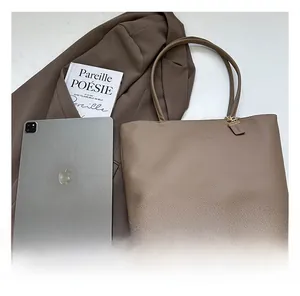 Detail view of a large camel tote bag next to an iPad showing its spacious capacity