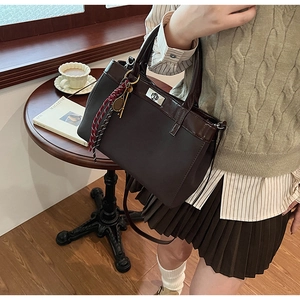 Detail shot of a coffee brown matte handbag with tennis racket charm and woven tassel