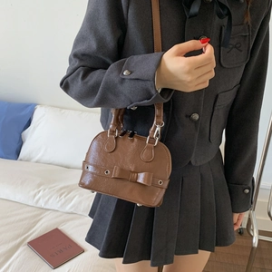 Close-up of a dark brown shell bag with a bow accent worn with a school style outfit