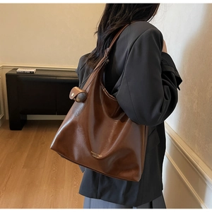Détail d'un sac cabas en cuir marron avec large bandoulière nouée et logo doré