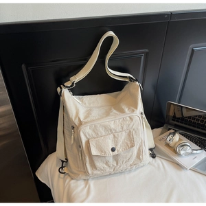 Detail of off-white nylon tote showing pleated fabric and silver metal zipper compartments