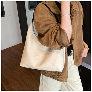 Close-up of beige textured canvas hobo bag with black shoulder strap worn by a model