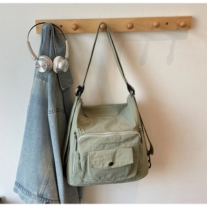Detail view of light green nylon multi-pocket tote bag hanging with denim jacket