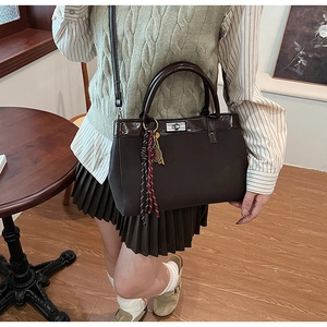 Detail of dark brown tote bag with metal twist lock and decorative woven pendant