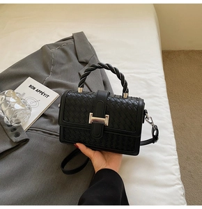 Detail of black woven texture handbag with silver H-shaped buckle and braided handle