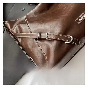 Detail view of brown vintage leather bag with contrast stitching and metal buckle