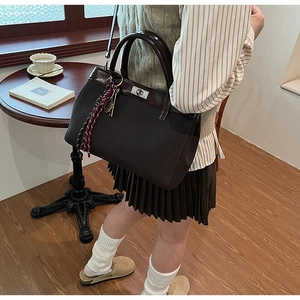 Detail of dark brown matte leather handbag with vintage silver lock and woven rope charm