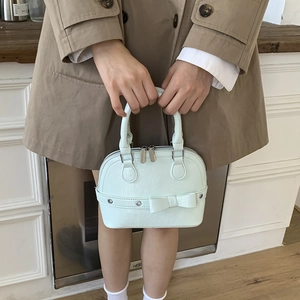 Close-up of light mint green shell bag with leather bow detail held by a model