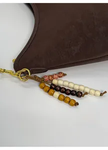 Detail of a brown leather shoulder bag featuring colorful wooden bead tassel charms