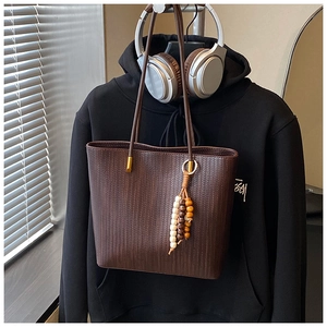 Dettaglio di una borsa tote marrone in pelle PU intrecciata con ciondolo in perle di legno