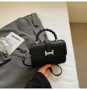 Detail of black woven texture handbag with silver H buckle and twisted handle design