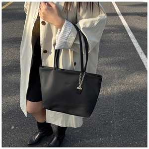 Detail of classic black tote bag in lychee leather with gold chain and beige trench coat