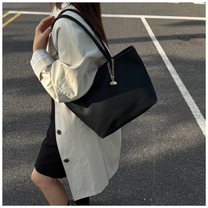 Close-up of black pebble leather tote bag with gold chain detail and shoulder strap