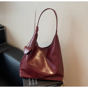 Détail du sac hobo en cuir bordeaux sur un canapé noir avec un livre de décoration