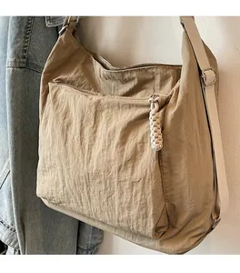 Detail of khaki nylon shoulder bag featuring large front zipper pocket and woven puller