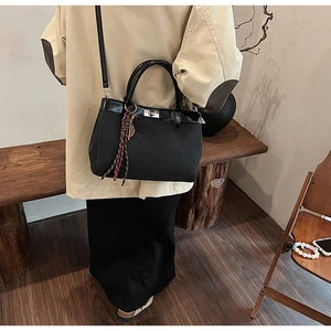 Detail of black matte crossbody bag with silver twist lock and decorative scarf on handle