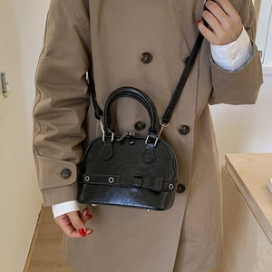 Detail of black shell bag with crocodile texture and bow decoration on trench coat