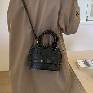 Side view of black vintage shell bag with bow detail worn over a khaki trench coat