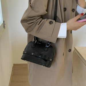 Detail of black shell crossbody bag with metal eyelets and bow detail on a trench coat