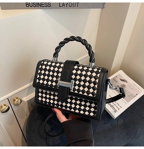 Detailed view of black and white checkered leather bag with silver H-shaped buckle