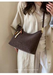 Detail of coffee brown crossbody bag featuring beaded charms and embossed logo patch