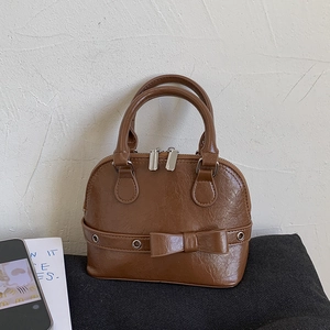 Close-up of brown glossy shell bag with bow detail and silver zipper in a lifestyle setting