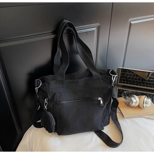 Close-up of black canvas tote bag with side coin purse and wide strap on white desk