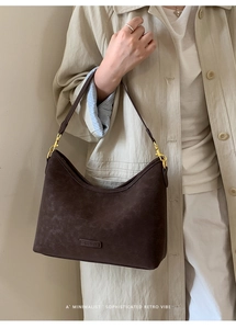 Close-up of vintage dark brown leather shoulder bag with gold hardware on beige coat
