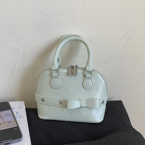 Detail view of mint green shell bag featuring decorative bow and metallic eyelets
