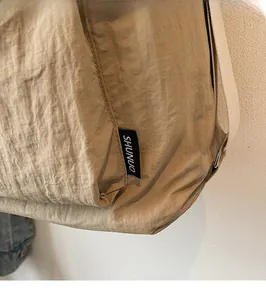 Close-up of khaki nylon messenger bag fabric with SHUNUO brand label and waterproof texture