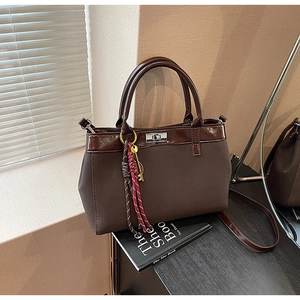 Detail of dark brown handbag with silver twist lock and woven key pendant on a book