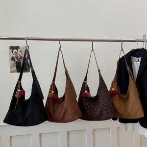 Détail de grands sacs hobo en daim givré avec pompons décoratifs sur cintres métalliques
