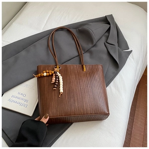 Dettaglio borsa tote intrecciata marrone con nappa di perline colorate e fibbie d'oro