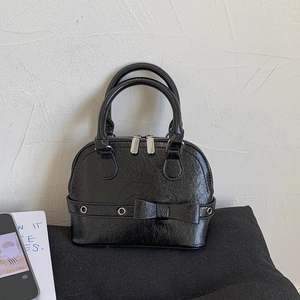 Detail of black oil wax texture shell bag with bow decoration and silver metal zipper
