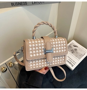 Detail of woven square bag with beige pattern, silver metal lock, and braided handle