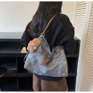 Detail of gray-blue washed canvas tote with leather strap and plush bear charm
