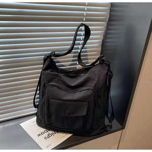 Close-up of black nylon tote bag showing front zipper pockets and flap pocket detail