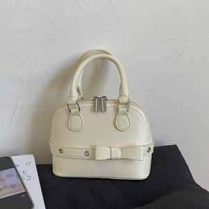 Close-up of beige shell bag featuring mini bow accent and metallic rivet details