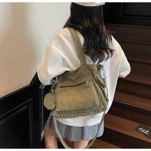Detail of army green canvas tote bag with side pouch shown on a model on stairs