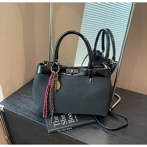 Detail of black patchwork tote with suede texture, metal charm and red braided rope trim