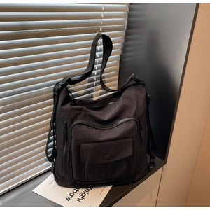 Detail of black nylon crossbody bag featuring utility zipper pockets and wide shoulder strap