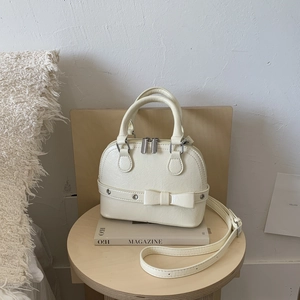Detail of a creamy beige shell bag with a bow accent and textured PU leather finish