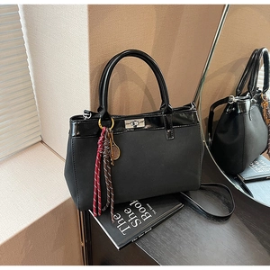 Detail of black matte tote with glossy trim, metal clasp, and tassel tennis charm