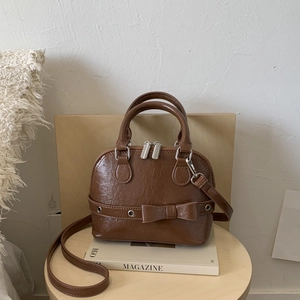 Macro view of brown shell-shaped crossbody bag with glossy faux leather and bow detail